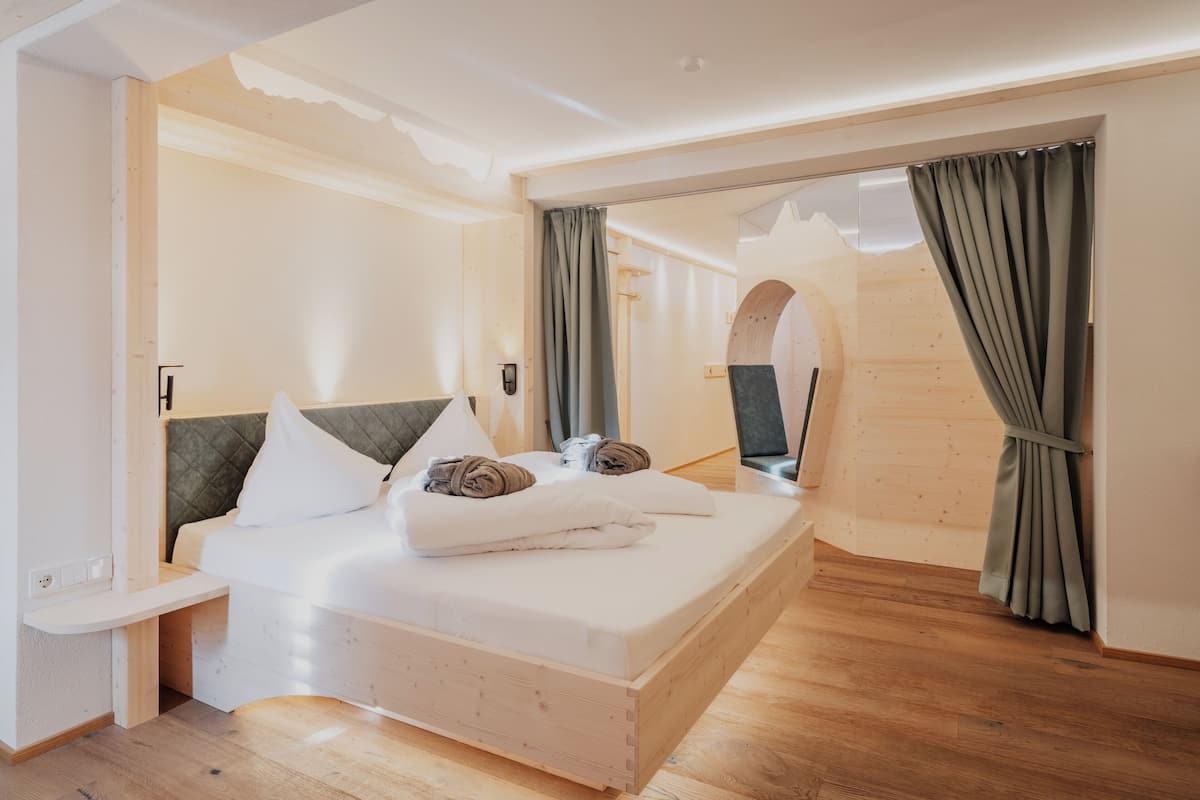 Ein modernes Hotelzimmer mit einem hölzernen Bett, einem Nachttisch und Blick durch eine geöffnete Tür.