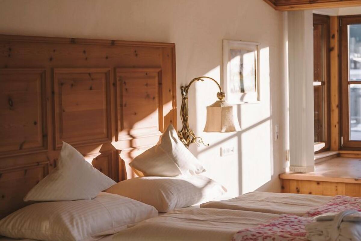 Ein Schlafzimmer mit Holzkopfstütze, einem Bett mit weißer Bettwäsche, einem Nachttisch mit Lampe und einem Fenster mit Blick.