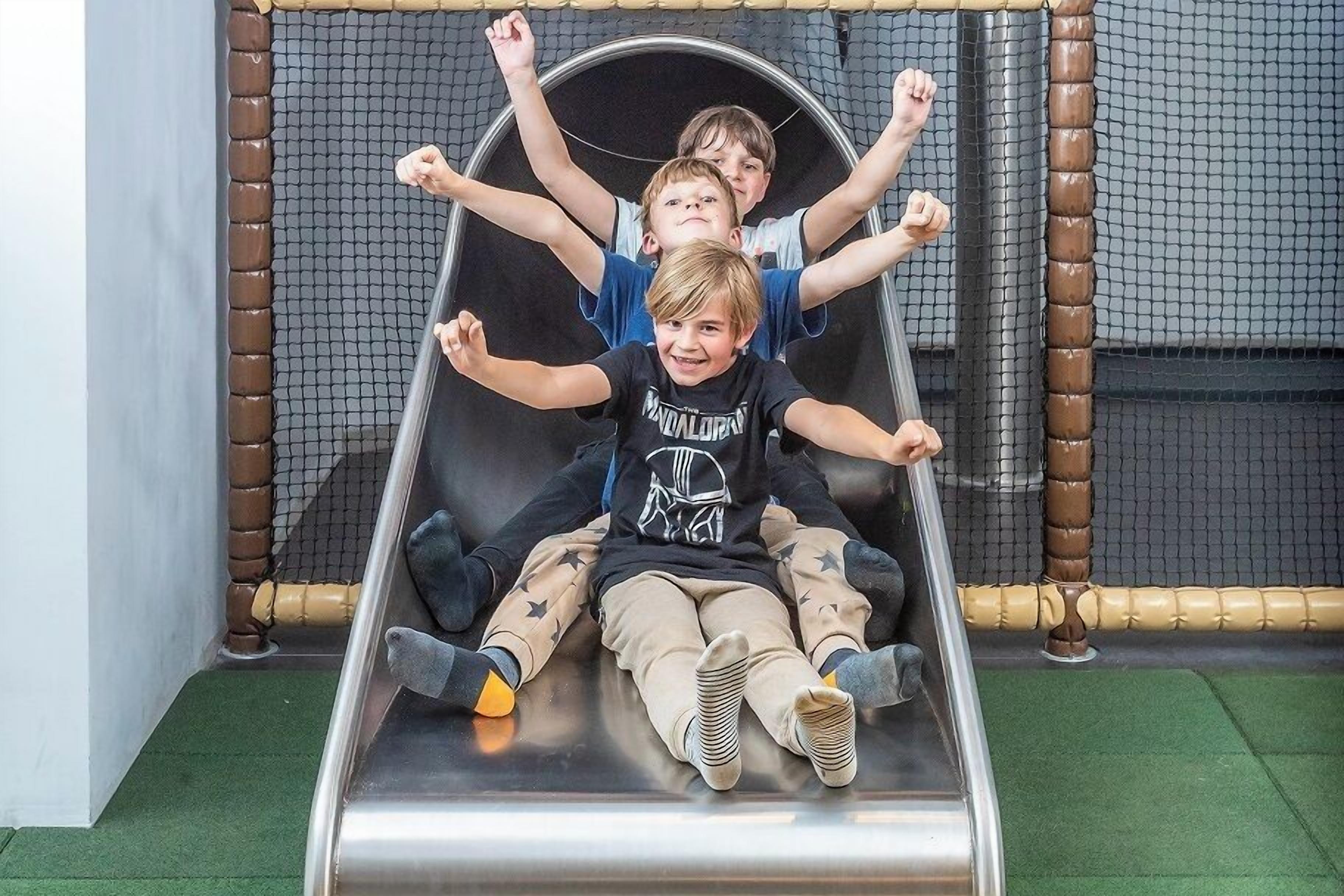 Eine Rutsche mit Kindern oben, einem Netz und einem grünen Boden.