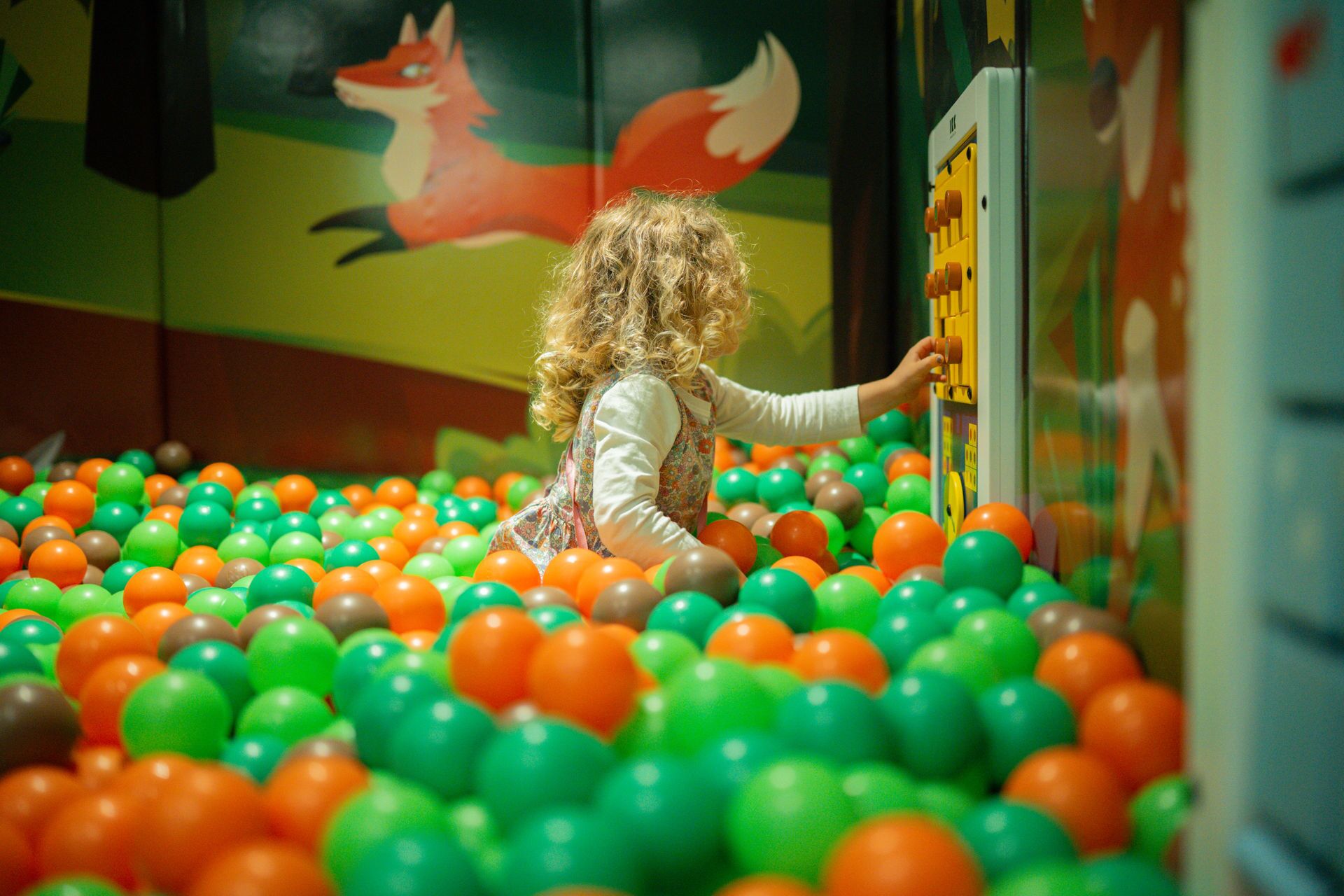 A child playing in a ball pit with colorful balls.