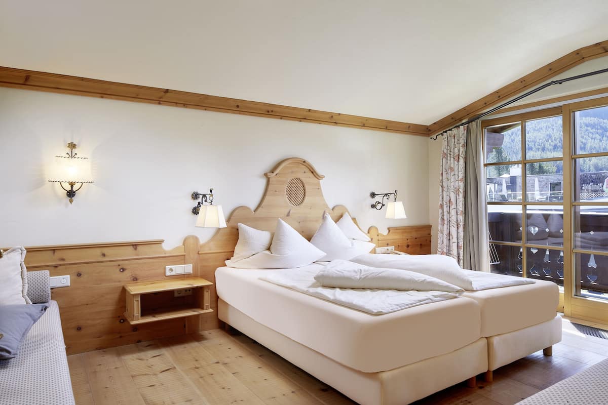 Ein Schlafzimmer mit einem Holzkopfteil, einem großen Bett mit weißer Bettwäsche, zwei Nachttischen mit Lampen und Blick auf eine Berglandschaft durch ein großes Fenster.