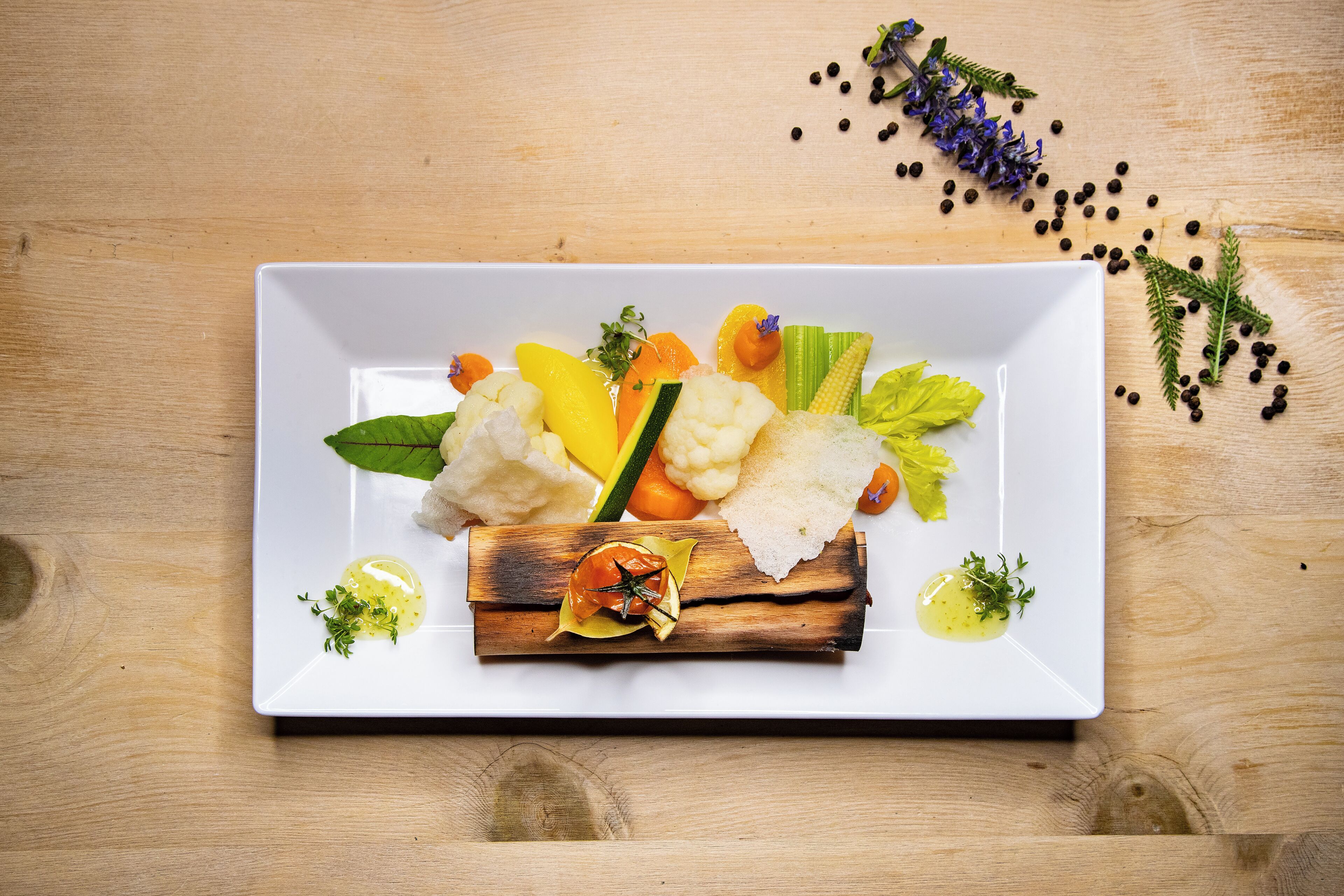 A white rectangular plate with a variety of vegetables and herbs on a wooden surface.