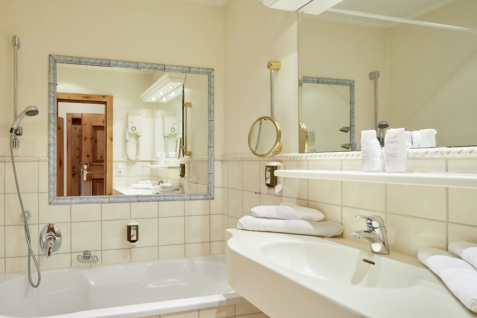 Een badkamer met een bad, twee wasbakken, een grote spiegel en een douche.