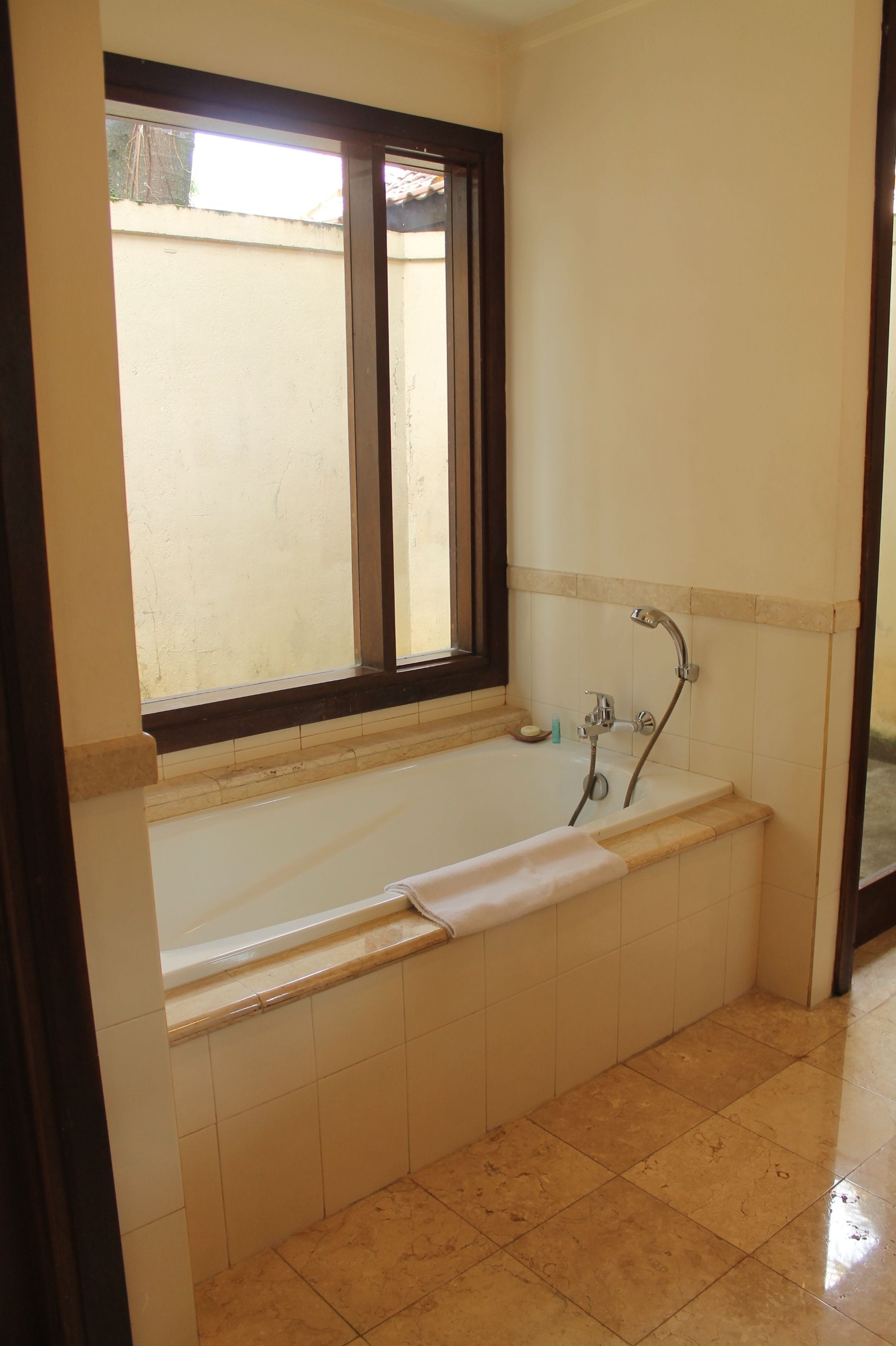 A bathroom with a bathtub, a window, and a tiled floor.