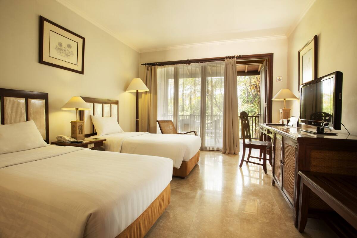 A hotel room with two beds, a desk with a television, and a chair.
