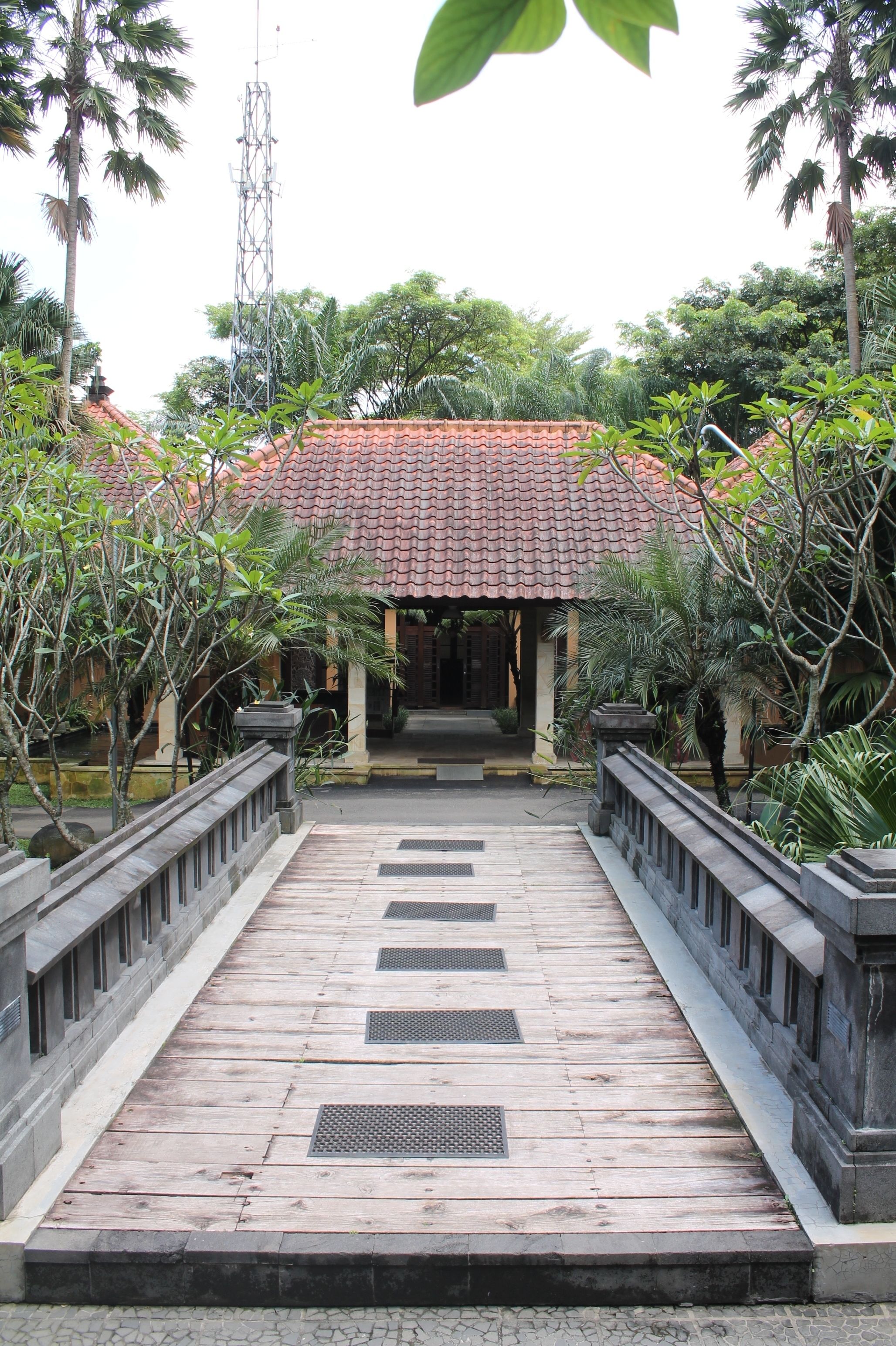 A traditional building with a tiled roof, surrounded by lush greenery and a stone pathway leading to the entrance.
