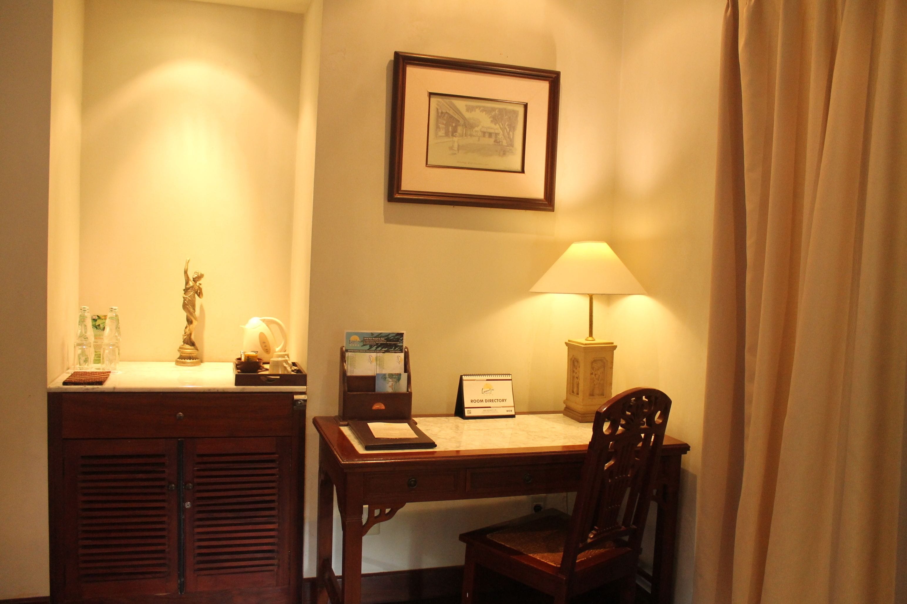 A room with a desk, chair, lamp, framed picture, and a 'Room Directory' sign.