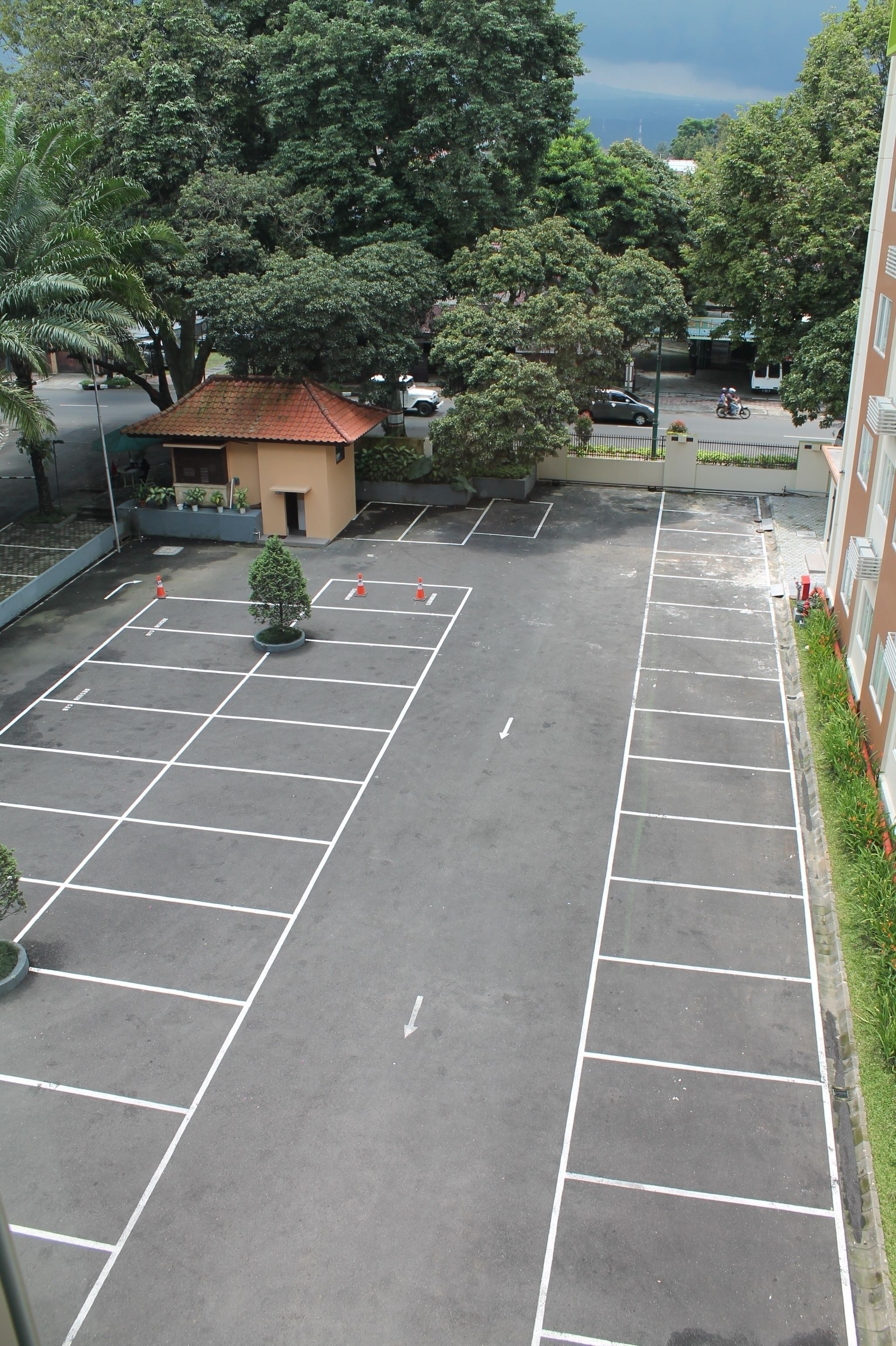 A parking lot with marked spaces, a small building with a red roof, and surrounding greenery.