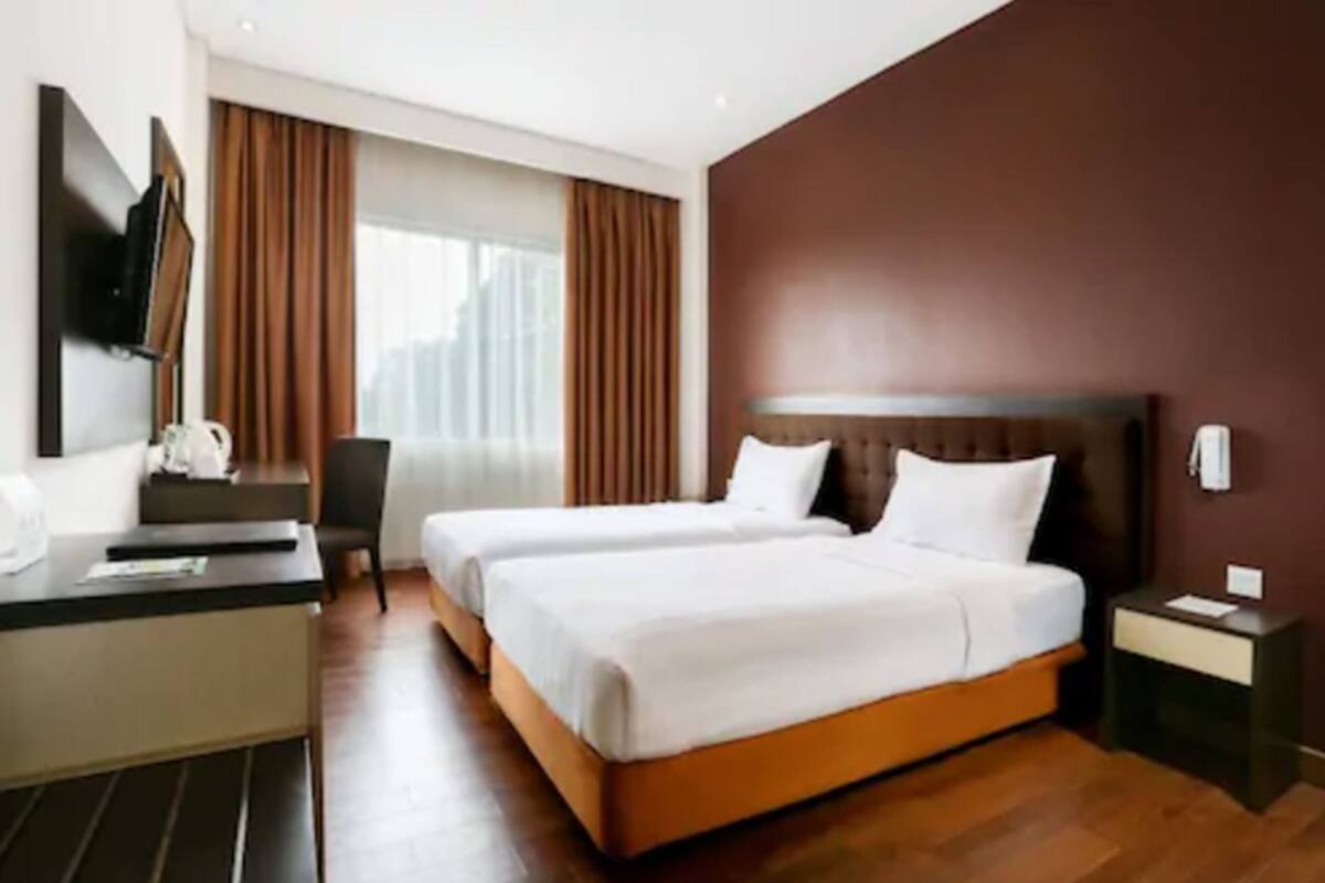 A hotel room with two beds, a desk, a chair, and a TV.