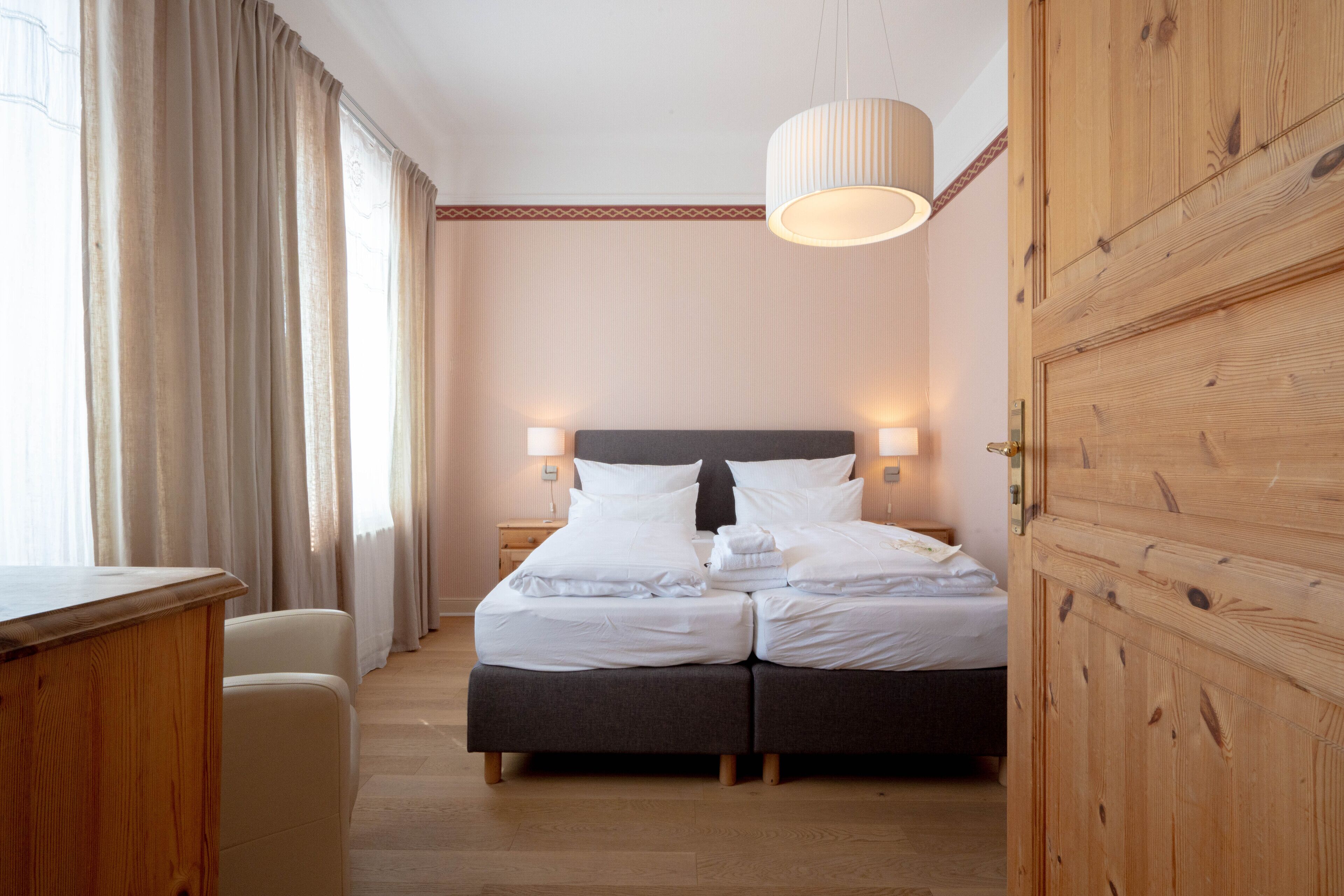 A hotel room with a double bed, bedside lamps, a wooden wardrobe, and a desk.