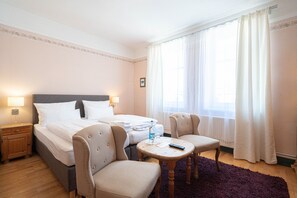 Una habitación de hotel con cama, dos sillones, una mesita y una mesita de noche.