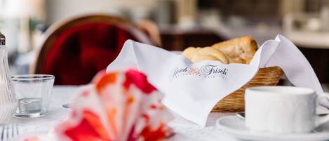 A dining table with a basket of bread, a cup, and a glass.