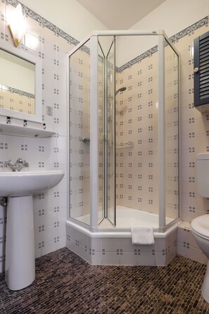 Un baño moderno con cabina de ducha de vidrio, un lavamanos blanco y azulejos estampados.