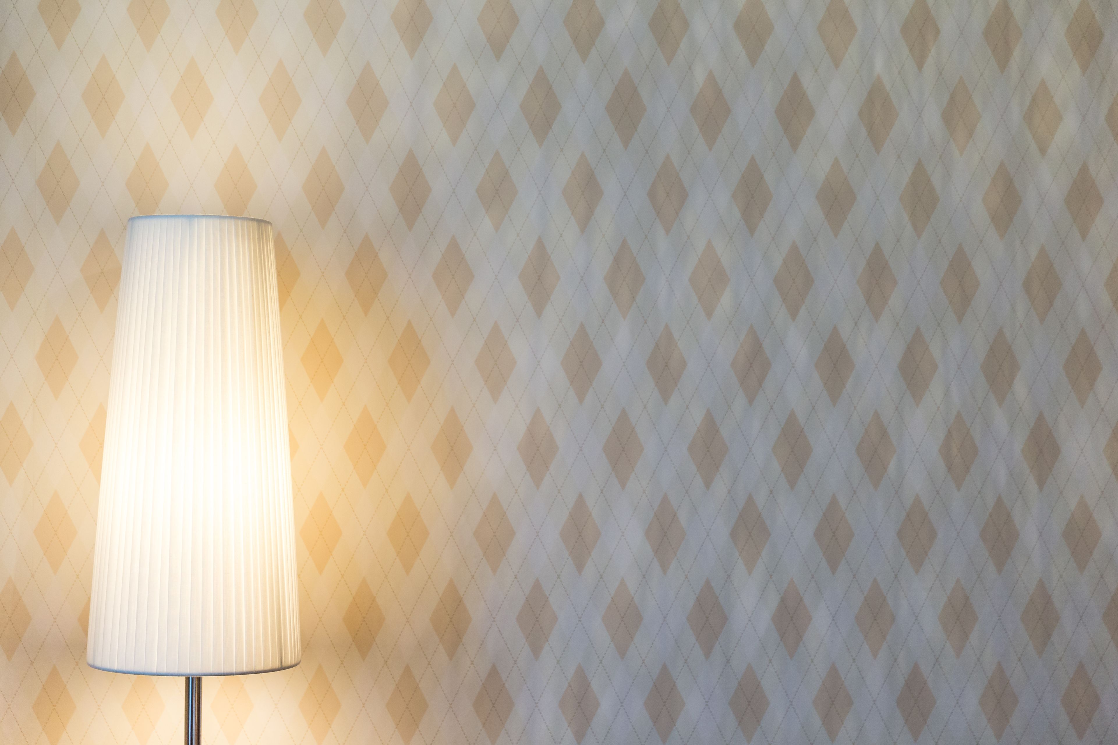 Een lamp met een geribbelde kap voor een behang met een diamantpatroon.