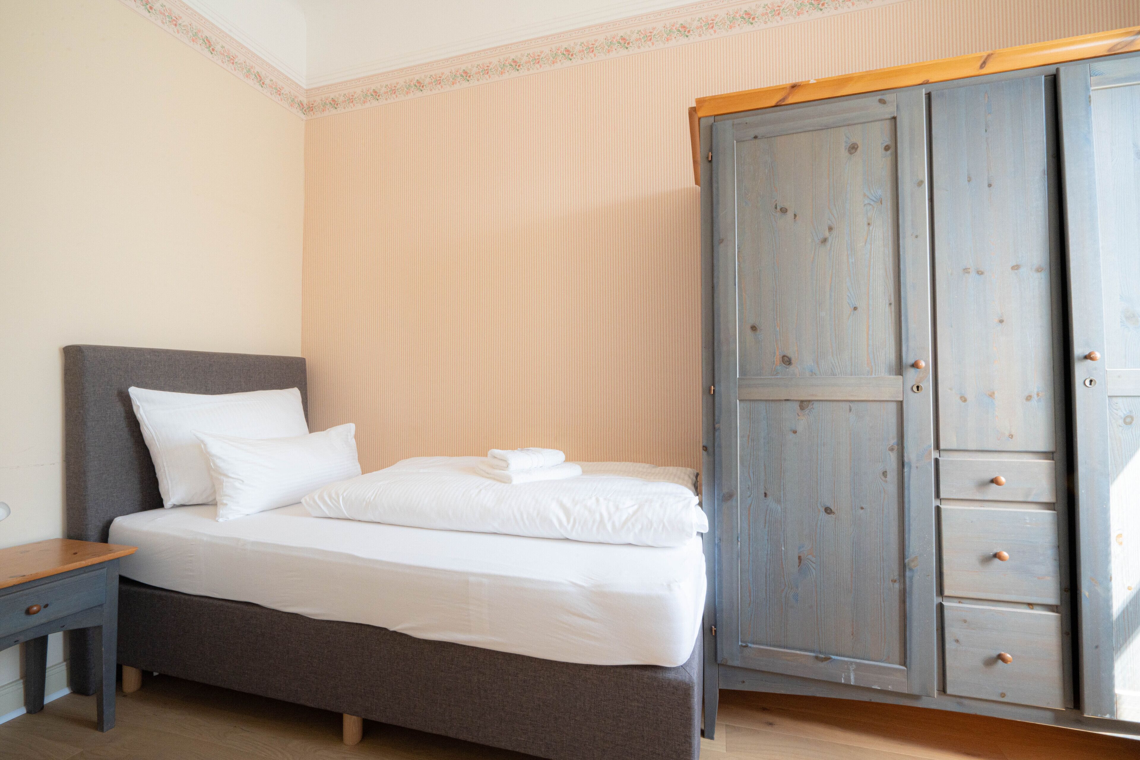 Un dormitorio con una cama, una mesita de noche de madera y un armario con varios cajones.