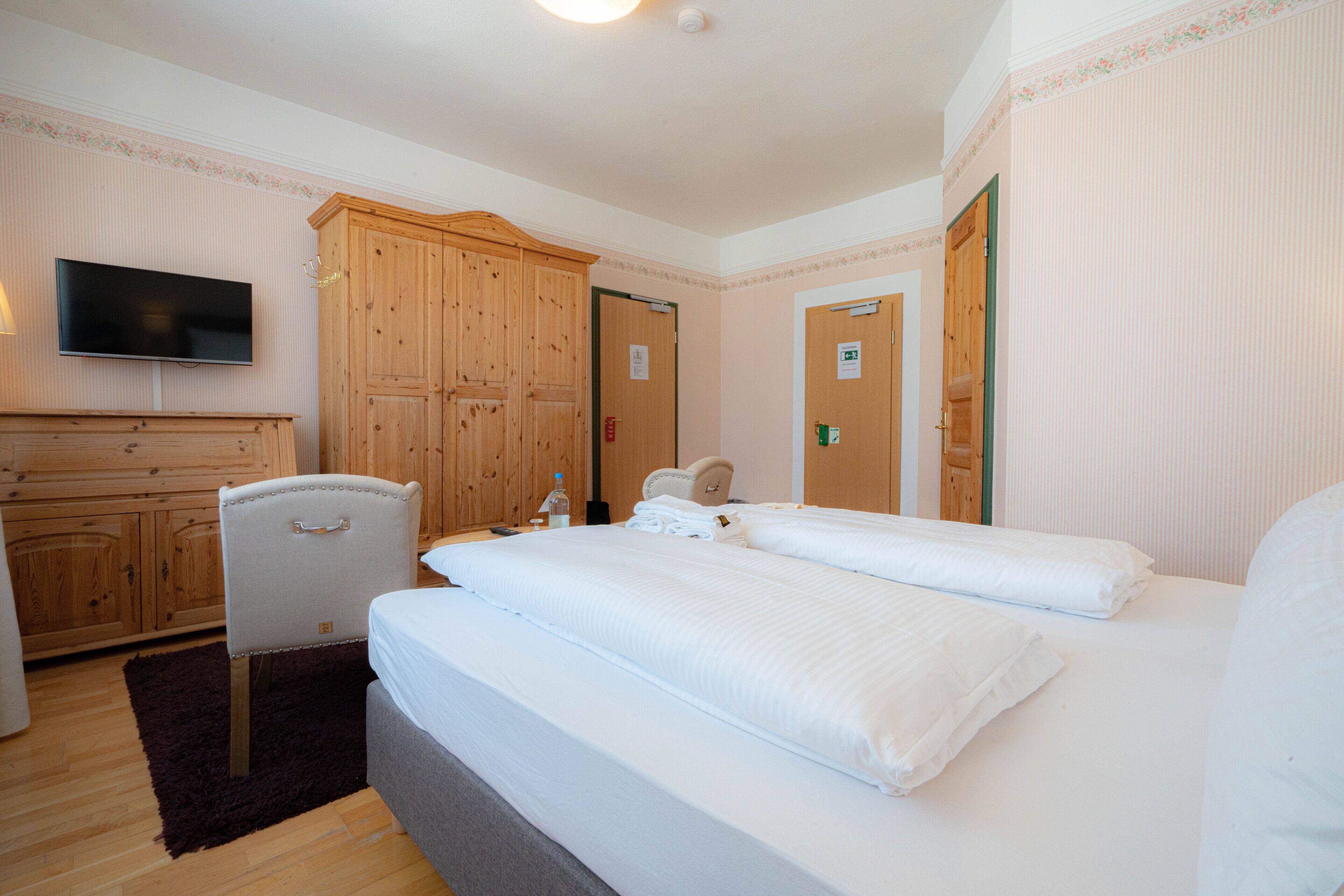 A hotel room with a large bed, a wooden wardrobe, a television, and a chair.