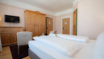 A hotel room with a large bed, a wooden wardrobe, a television, and a chair.