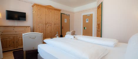Een hotelkamer met een groot bed, een houten garderobe, een televisie en een stoel.