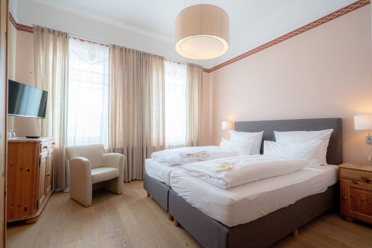 A hotel room with a bed, a TV, a chair, and a wooden cabinet.