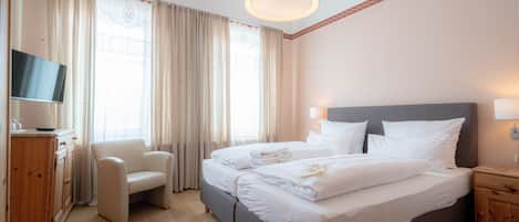 A hotel room with a bed, a TV, a chair, and a wooden cabinet.