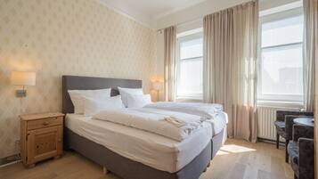 A hotel room with a large bed, two bedside tables, a small table with chairs, and a window with curtains.