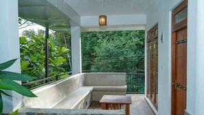 A balcony with a stone bench, a small table, and a view of lush greenery.