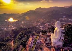 A large white statue on a hill overlooking a valley with a sunset in the background.