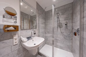 A modern bathroom with a glass-enclosed shower, a white sink, and a marble-tiled shower wall.