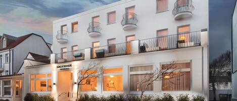 A multi-story hotel with balconies, a ground floor entrance, and a well-lit facade.