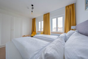 A hotel room with two beds, a chair, a window with curtains, and a radiator.