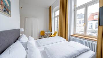 A hotel room with a bed, a desk, two chairs, a painting, and a window with curtains.