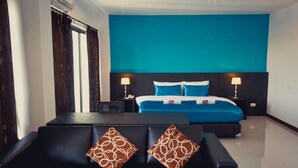 A hotel room with a large bed, two bedside tables with lamps, a sofa with patterned cushions, and a view of the city.
