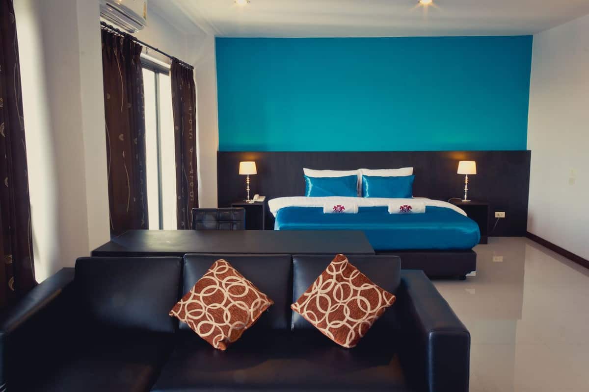 Habitación de hotel con una cama grande, dos mesitas de noche con lámparas, un sofá con cojines estampados y vistas a la ciudad.