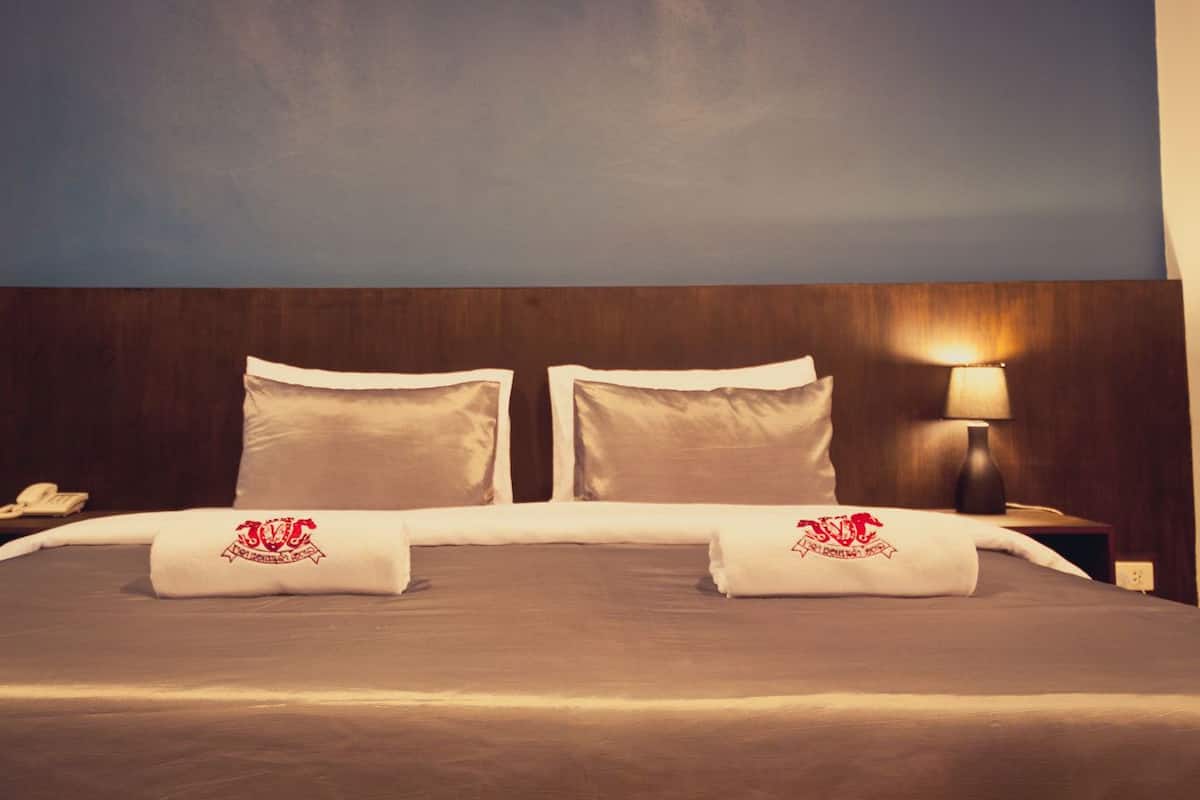 Habitación de hotel con una cama grande, dos almohadas, una lámpara de noche y una mesita de noche con un teléfono.