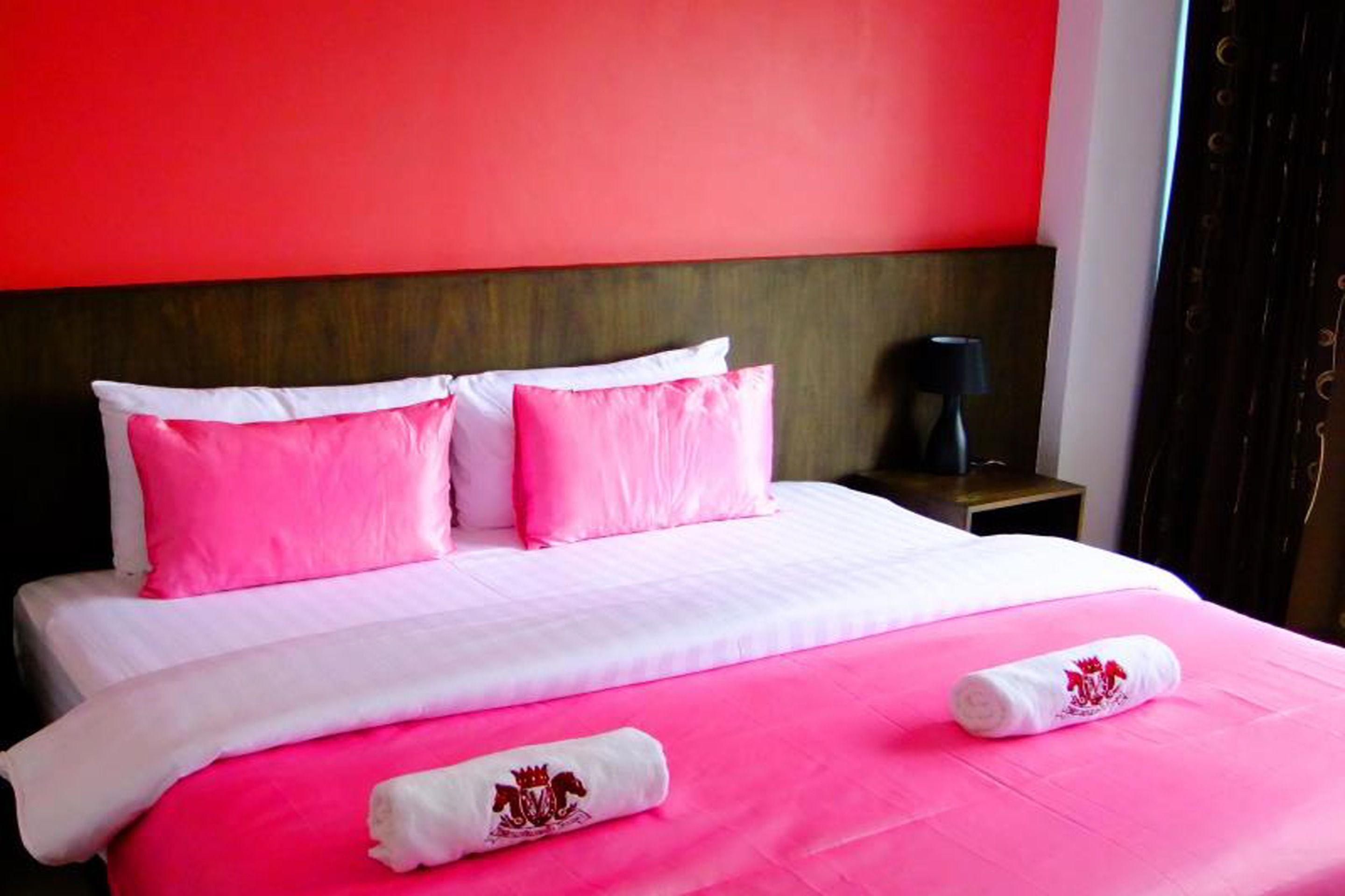 A hotel room with a bed featuring pink and white bedding, a wooden headboard, and a nightstand with a lamp.