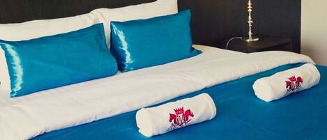 A neatly made bed with blue and white bedding, a nightstand with a lamp, and a blue wall.