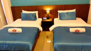 A hotel room with two beds, each with a blue bedspread and pillows, and a nightstand with a lamp between them.