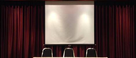A conference room with a large screen, a table, and chairs.