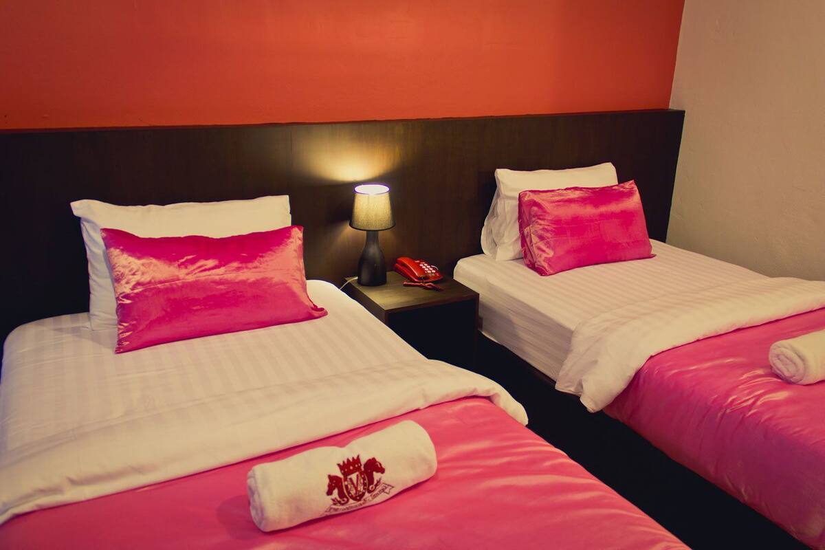 Dos camas individuales con ropa de cama rosa y una mesita de noche con una lámpara y un teléfono.