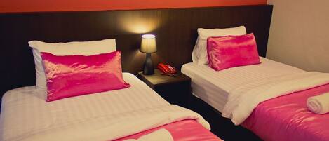 Two twin beds with pink bedding and a nightstand with a lamp and a phone.
