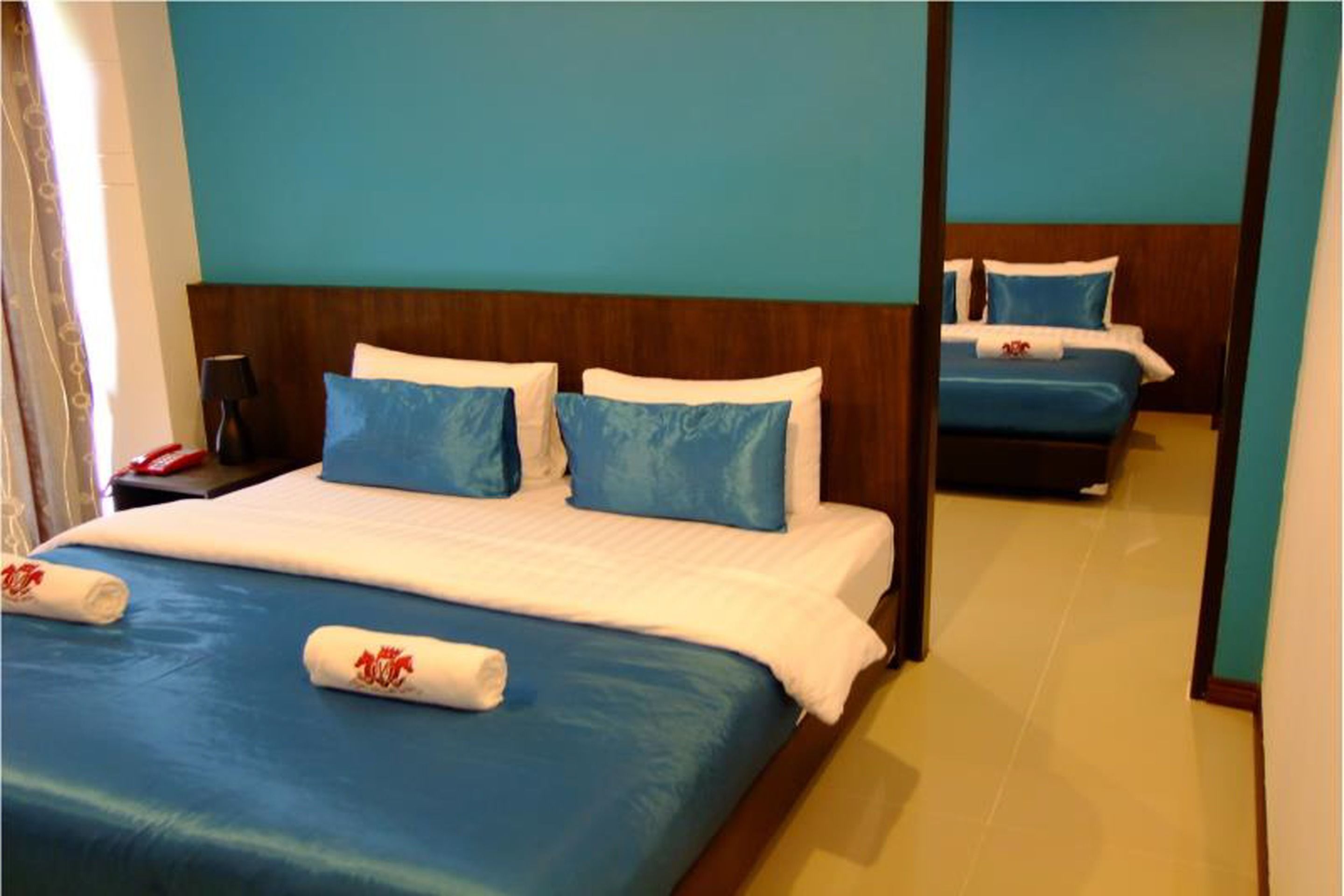 A hotel room with a large bed, a smaller bed in the background, and a wooden headboard.