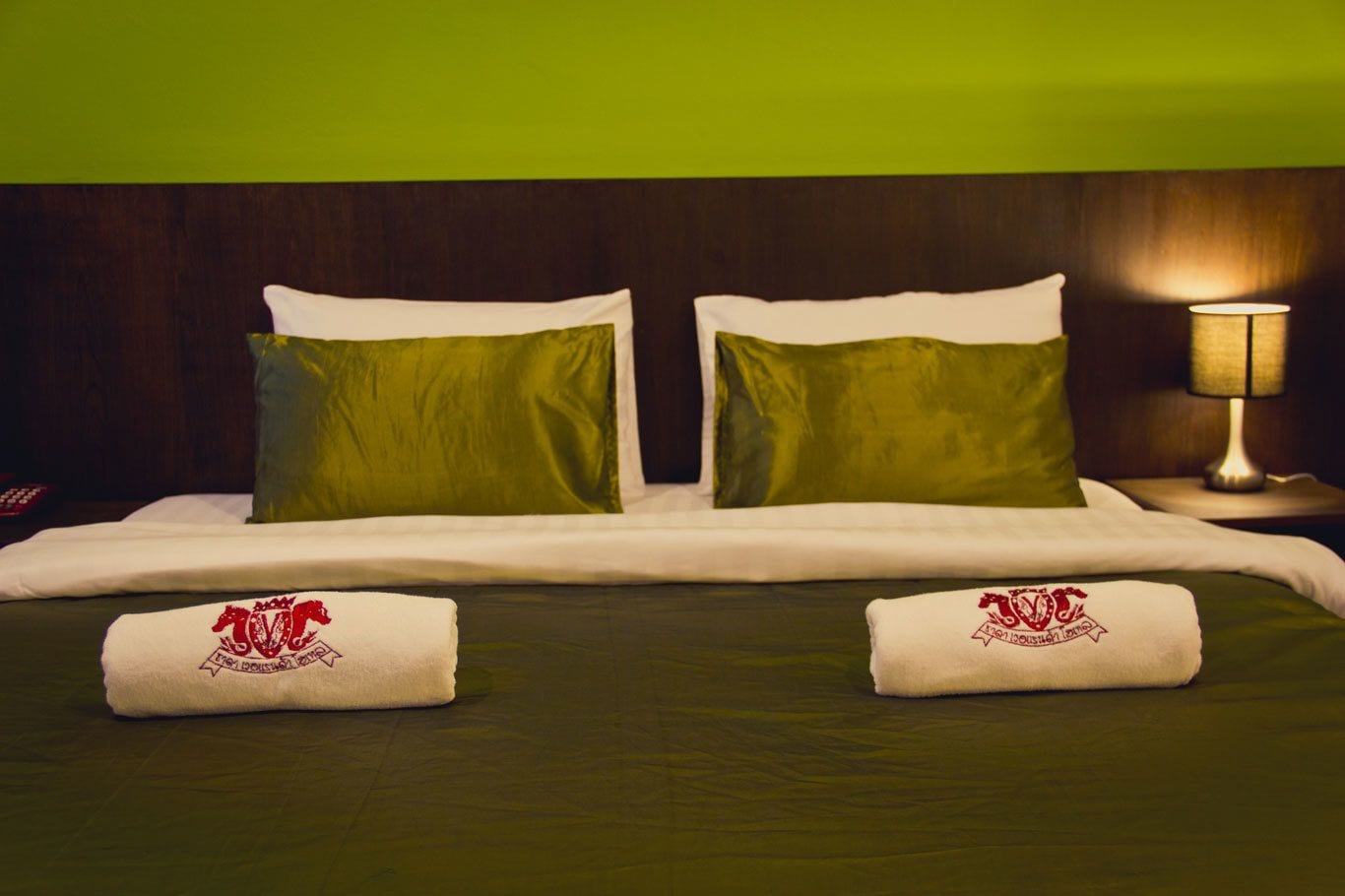 A neatly made bed with green and white bedding, two pillows, and two towels with a logo.