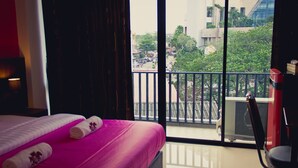 A hotel room with a large bed, a chair, and a balcony with a view of buildings and trees.