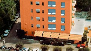 Un edificio de varios pisos con techo plano, rodeado de árboles y una playa.