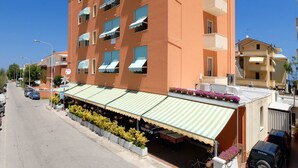 Un hotel de varios pisos con balcones, una zona de estar al aire libre techada y un cielo azul despejado.