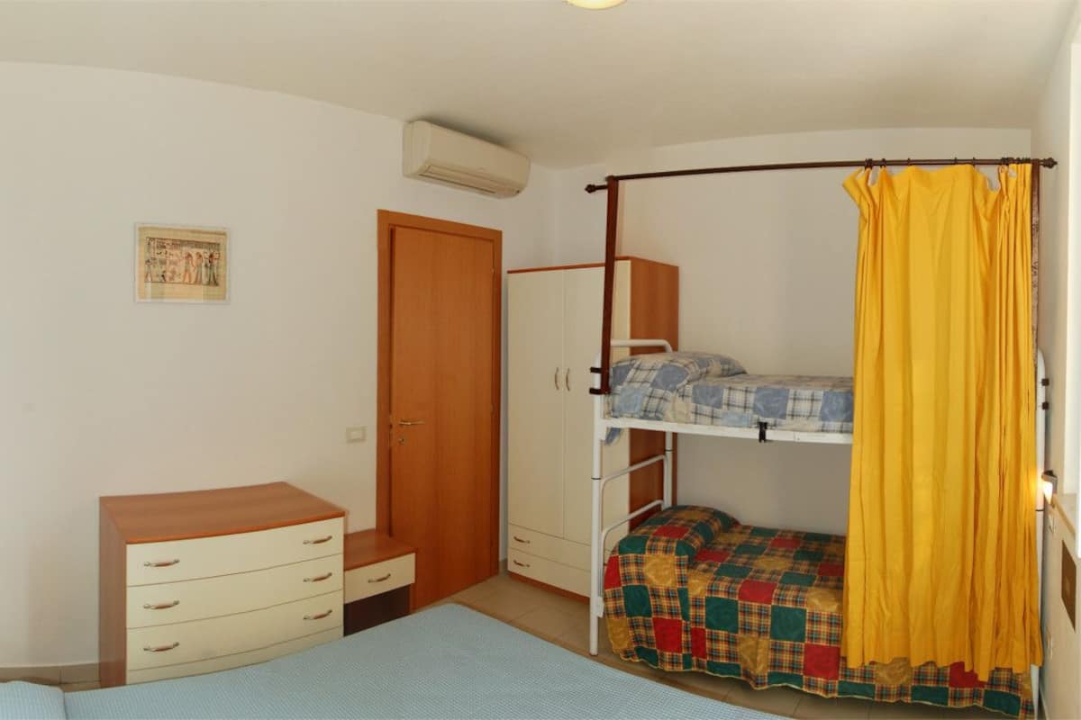 A bedroom with a bunk bed, a wooden dresser, a wardrobe, and a single bed.