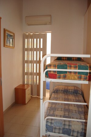 Camera con letto a castello, un armadietto in legno e una finestra con persiane.