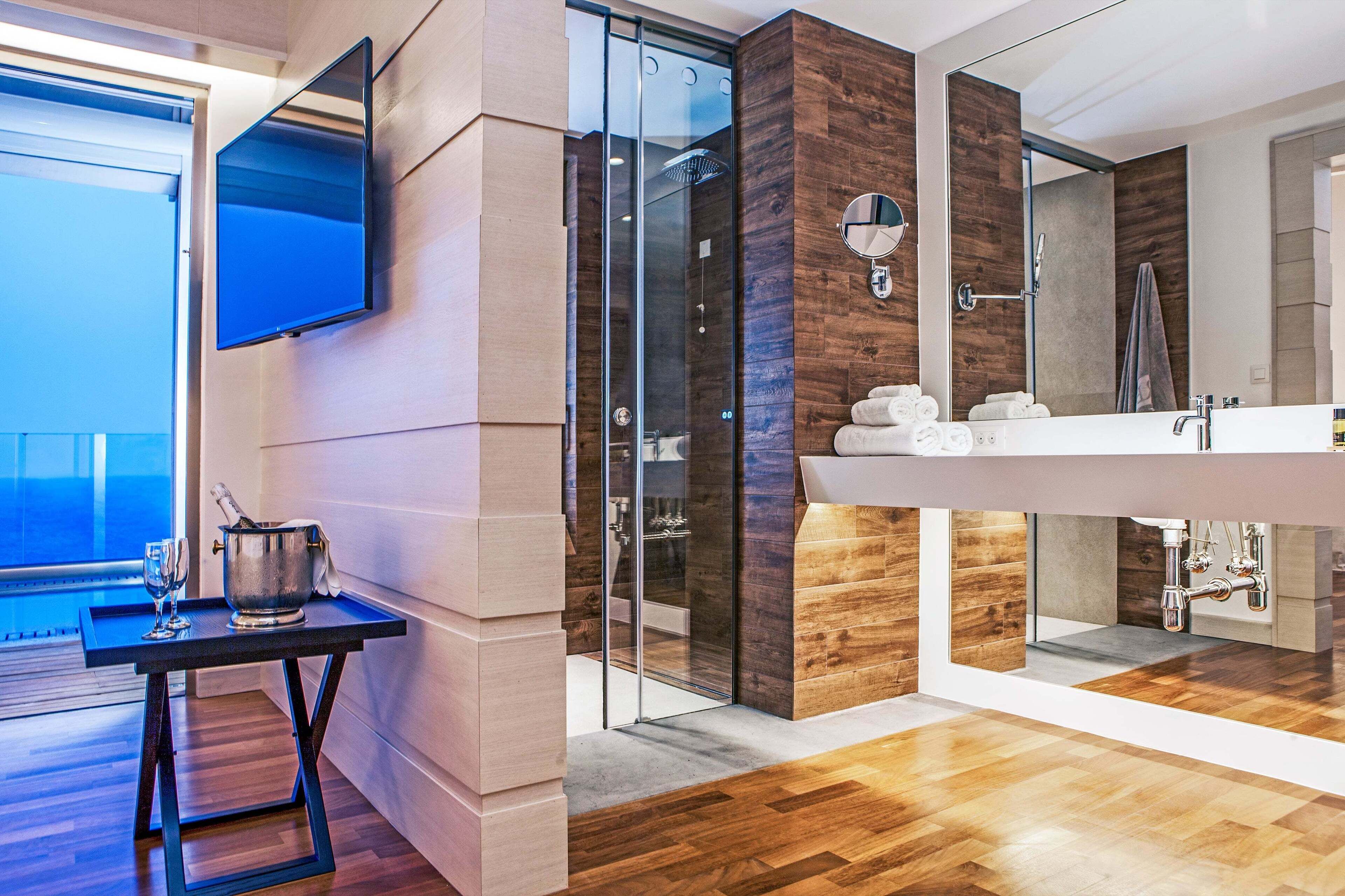 A modern bathroom with a large mirror, a glass shower enclosure, and a wooden floor.