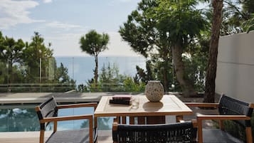 A wooden table with chairs, a vase, and books, overlooking a swimming pool and a view of the sea.