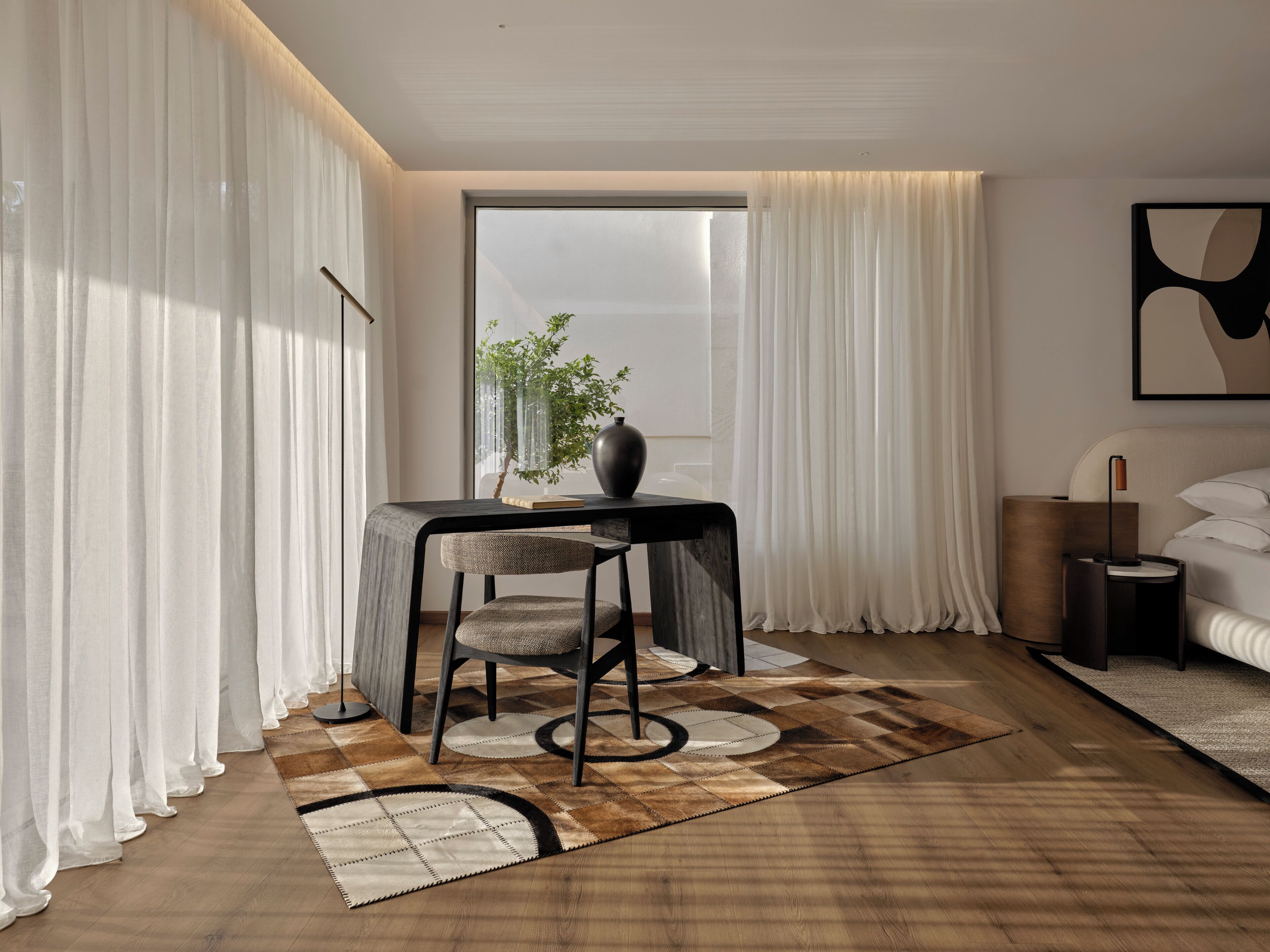 Ein modernes Hotelzimmer mit Essbereich, einem großen Fenster mit Vorhängen, einer Zimmerpflanze und einem Bett mit Kopfteil.